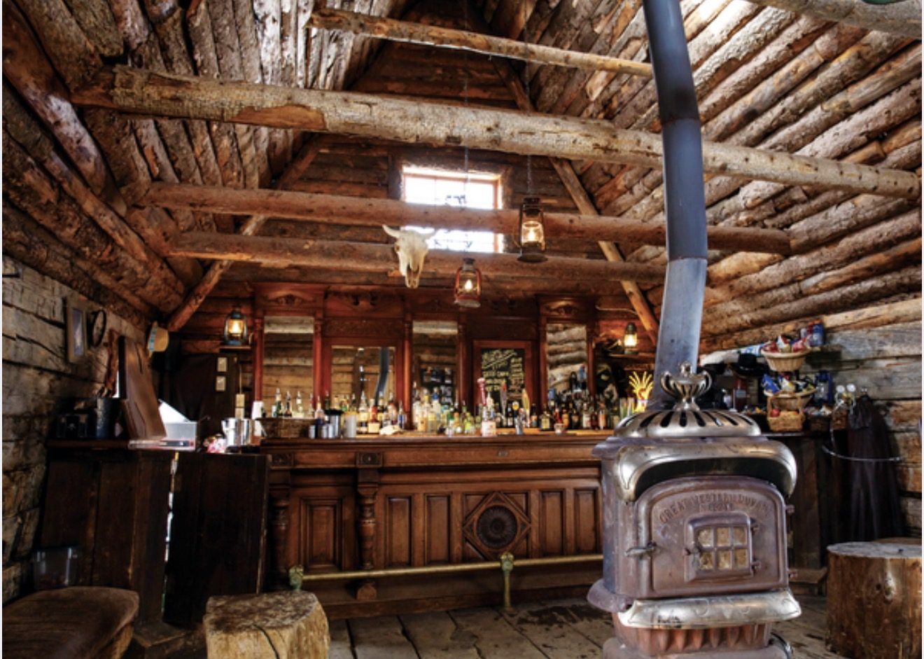 Inside the historic Gorrono Saloon, log walls and beams, lanterns, a carved back bar and a wood stove