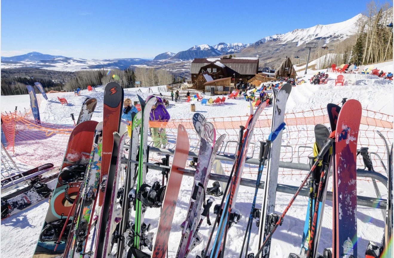 Skis and snowboards racked outside Gorrono Ranch with the lodge and the mountains behind