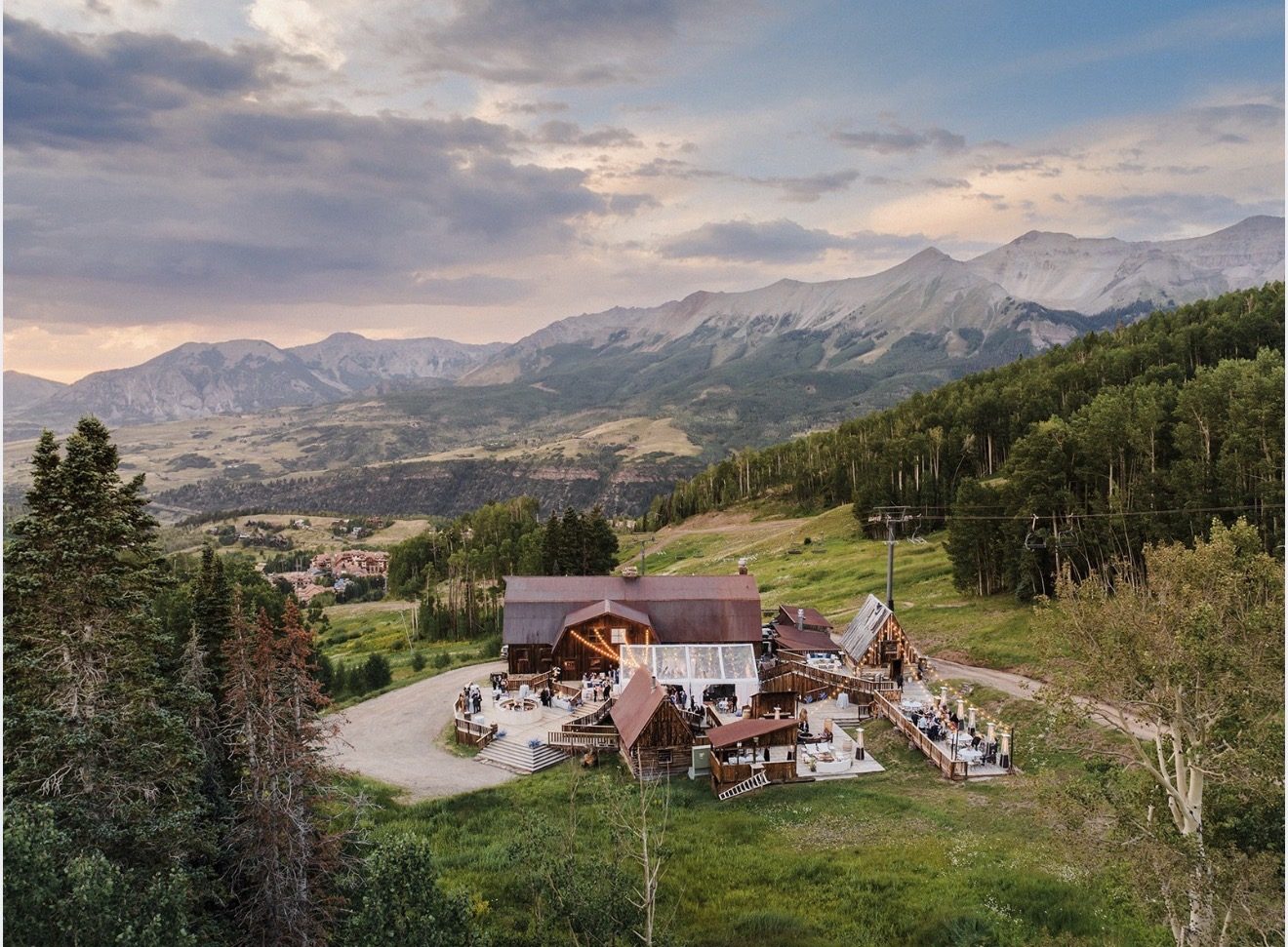 Gorrono Ranch from above on a summer evening, an event under string lights on the decks with the San Juan mountains and the valley beyond