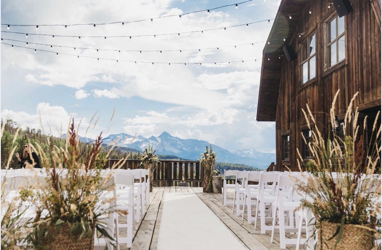 A summer wedding ceremony set up on the Gorrono Ranch deck, white chairs either side of the aisle with the San Juan mountains beyond